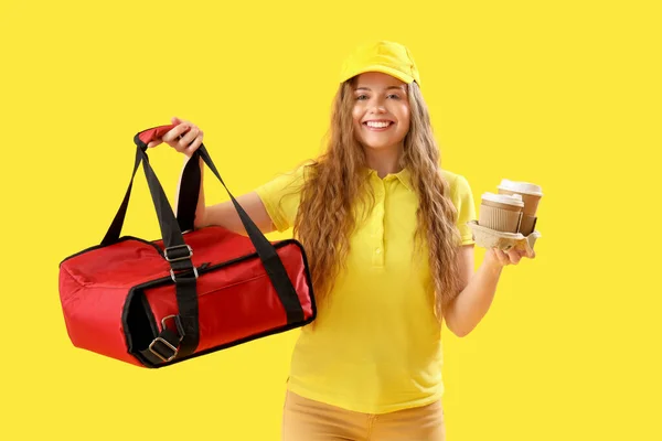 Female courier with thermal bag and cups on yellow background