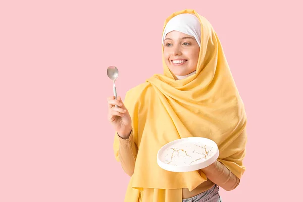 ピンクの背景に空のプレートとスプーンを持つ美しいアラビアの女性 — ストック写真