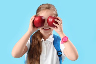 Açık mavi arka planda elmaları olan komik küçük okul kızı.