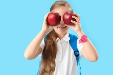 Açık mavi arka planda elmaları olan komik küçük okul kızı.