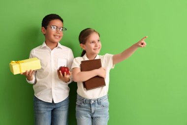 Yeşil arka planda kitabı, hediyesi ve elması olan küçük öğrenciler