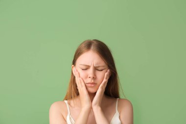 Yeşil arka planda diş ağrısı çeken genç bir kadın.