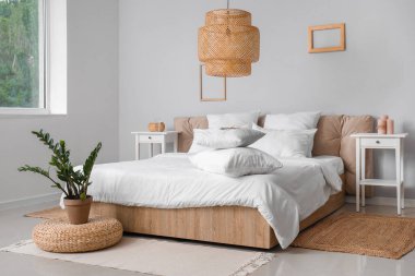 Konforlu çift kişilik yatak odası, beyaz yastıklar, çiçek ve hasır lamba.