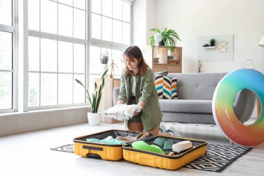 Evdeki bavuldan plaj havlusunu çıkaran genç bir kadın.