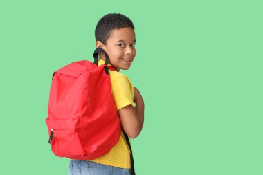 Yeşil arka planda okul çantası olan küçük Afro-Amerikalı çocuk.