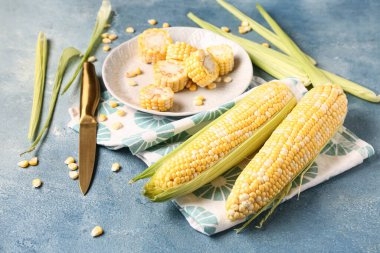 Mavi arka planda taze mısır koçanı ve tohumlu bir tabak.