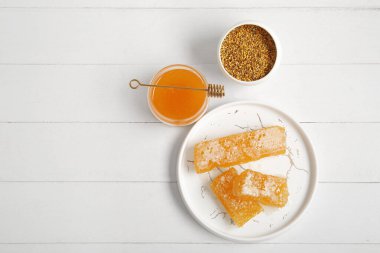 Bir kavanoz bal, tatlı taraklar ve hafif ahşap arka planda arı poleni