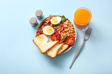 Lezzetli İngiliz kahvaltısı tabağı ve mavi arka planda bir bardak meyve suyu.