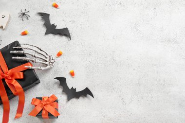 Hediye kutuları, lezzetli mısır şekerlemeleri, iskelet eller ve arka planda Cadılar Bayramı dekoru olan kompozisyon