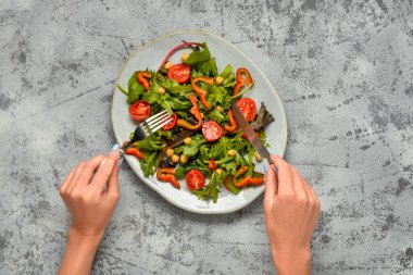 Gri arka planda taze sebze salatası yiyen kadın.