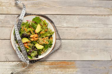 Taze salatalı tabak ve gri ahşap arka planda mezura. Diyet kavramı