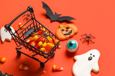 Kırmızı arka planda Cadılar Bayramı için lezzetli mısır ve kurabiyeli alışveriş arabası.