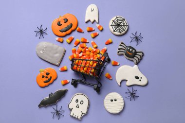 Mor arka planda Cadılar Bayramı için lezzetli mısır ve kurabiyeli alışveriş arabası.