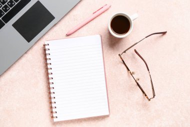 Dizüstü bilgisayarlı defter ve pembe arka planda bir fincan lezzetli kahve.