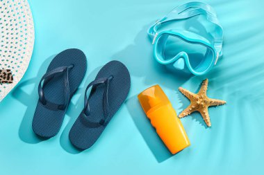 Güneş kremi ve mavi arka planda şnorkelli kadın tarzı terlikler.