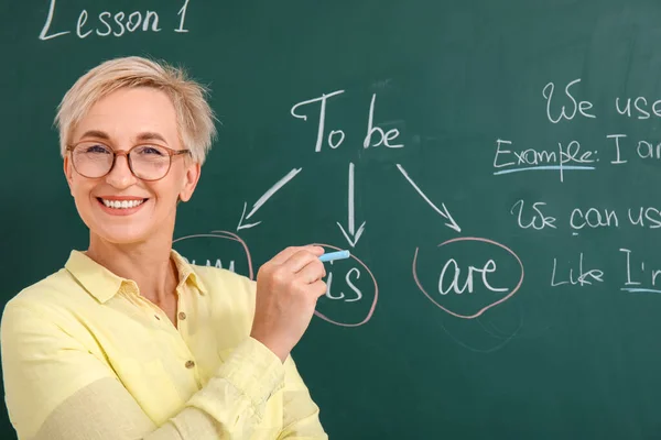 Female teacher writing English grammar on chalkboard in classroom, closeup