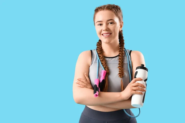 Sporty young woman with skipping rope and bottle of water on blue background