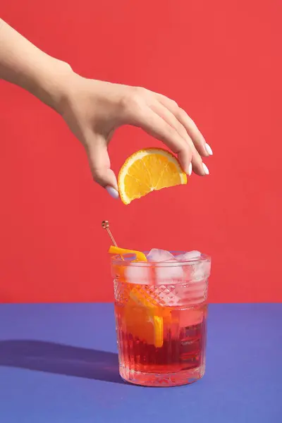 Frau Legt Orangenscheibe Glas Mit Negroni Cocktail Auf Farbigem Hintergrund — Stockfoto