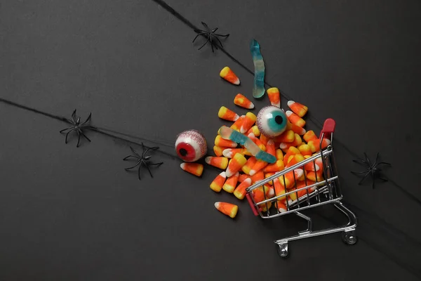 Shopping cart with tasty candy corns for Halloween on black background
