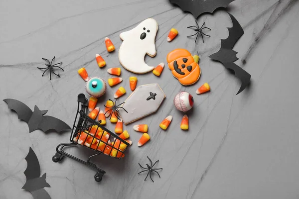 Shopping cart with tasty candy corns and cookies for Halloween on grey background