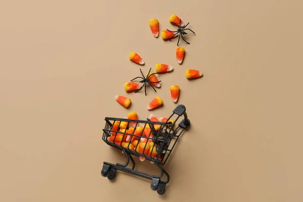 Shopping cart with tasty candy corns and Halloween decor on beige background