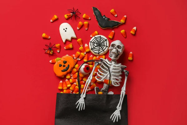 Shopping cart with tasty candy corns, skeleton and cookies for Halloween on red background