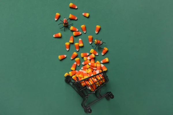 Shopping cart with tasty candy corns and Halloween decor on green background