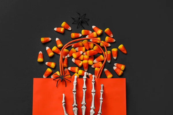 Shopping bag with tasty Halloween candy corns and skeleton hand on black background