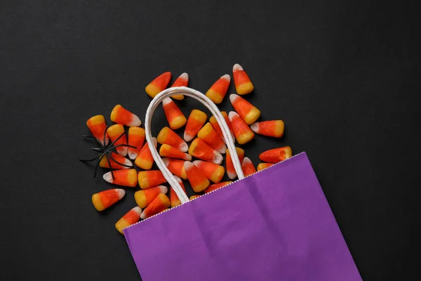 Shopping bag with tasty candy corns and Halloween decor on black background