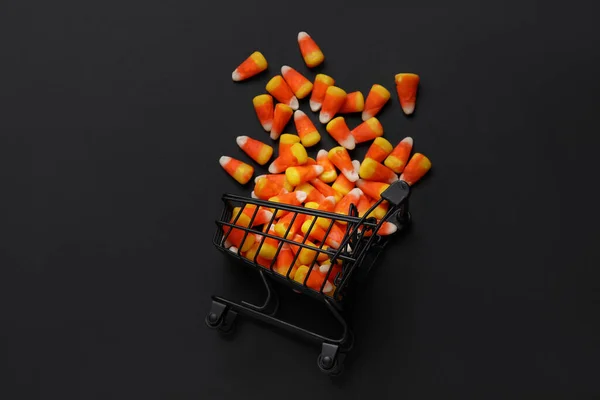 Shopping cart with tasty Halloween candy corns on black background