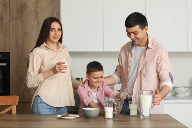 Mutfakta süt ve mısır gevreğiyle kahvaltı yapan mutlu bir aile.