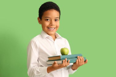 Yeşil arka planda kitapları ve elması olan küçük Afro-Amerikalı okul çocuğu.