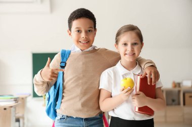 Sınıfta elma ve kitap taşıyan küçük öğrenciler.