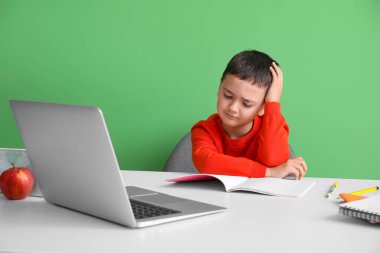 Stresli küçük çocuk yeşil duvarın yanındaki masada ödev yapıyor.