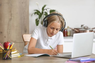 Kulaklıklı küçük çocuk mutfakta ödev yapıyor.