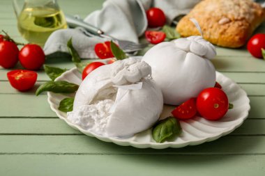 Yeşil ahşap arka planda lezzetli Burrata peyniri tabağı.