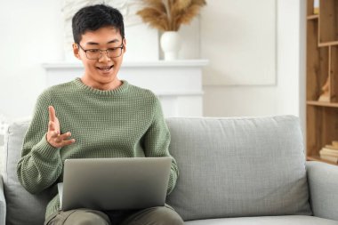 Evde dizüstü bilgisayarlı genç Asyalı sohbet ediyor.