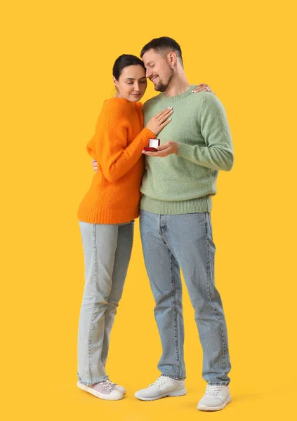 Young man proposing to his girlfriend on yellow background