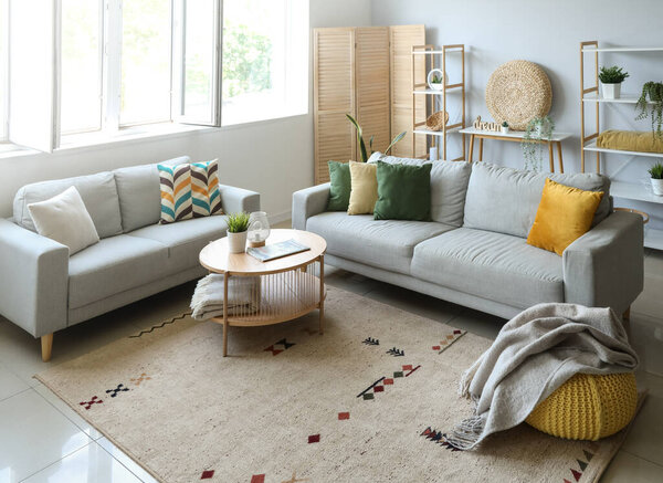 Cozy grey sofas and pouf with soft blanket in interior of light living room