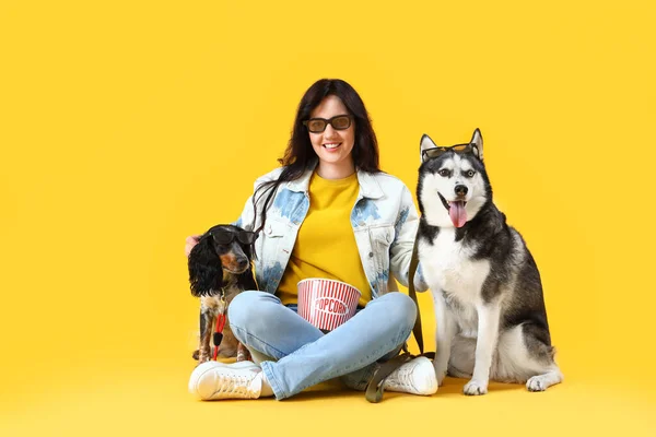 Young woman with cute dogs watching movie on yellow background