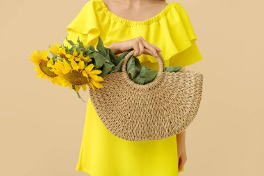 Bej arka planda güzel ayçiçekleri olan hasır çanta tutan kadın.