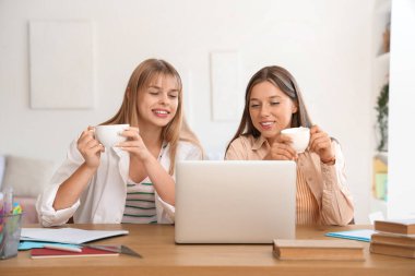 Elinde kahve fincanları olan kız öğrenciler yurt odasındaki masada ders çalışıyorlar.