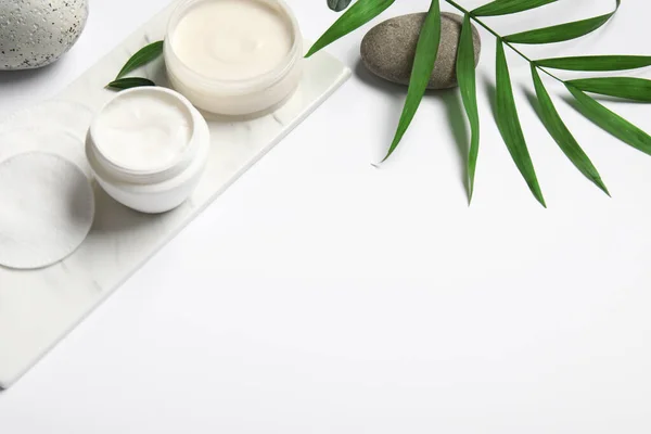 Jars of cosmetic products, cotton pads and palm leaf on white background