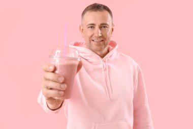 Pembe arka planda bir bardak meyve püresi olan olgun bir adam.