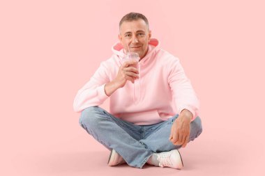 Pembe arka planda oturmuş meyveli buzlu içecek içen olgun bir adam.