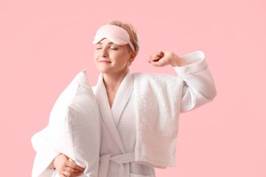 Pembe arka planda yastıklı, uyku maskeli genç kadın.