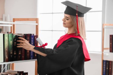 Female graduate student with diploma taking book from shelf in library clipart