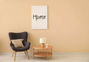 Gri koltuk ve bej duvarın yanındaki kahve masası. Posterli.