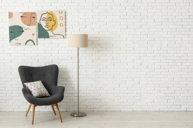 Beyaz tuğla duvarın yanındaki gri koltuk ve lamba.
