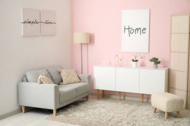 Oturma odasının içi rahat gri kanepe, beyaz dolap ve posterlerle dolu.